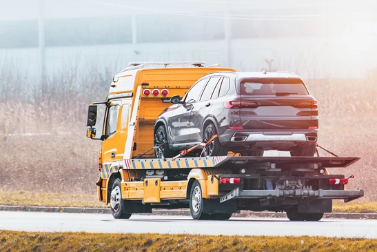 Scène extérieure sur route avec dépanneuse orange transportant un SUV gris sur plateau inclinable