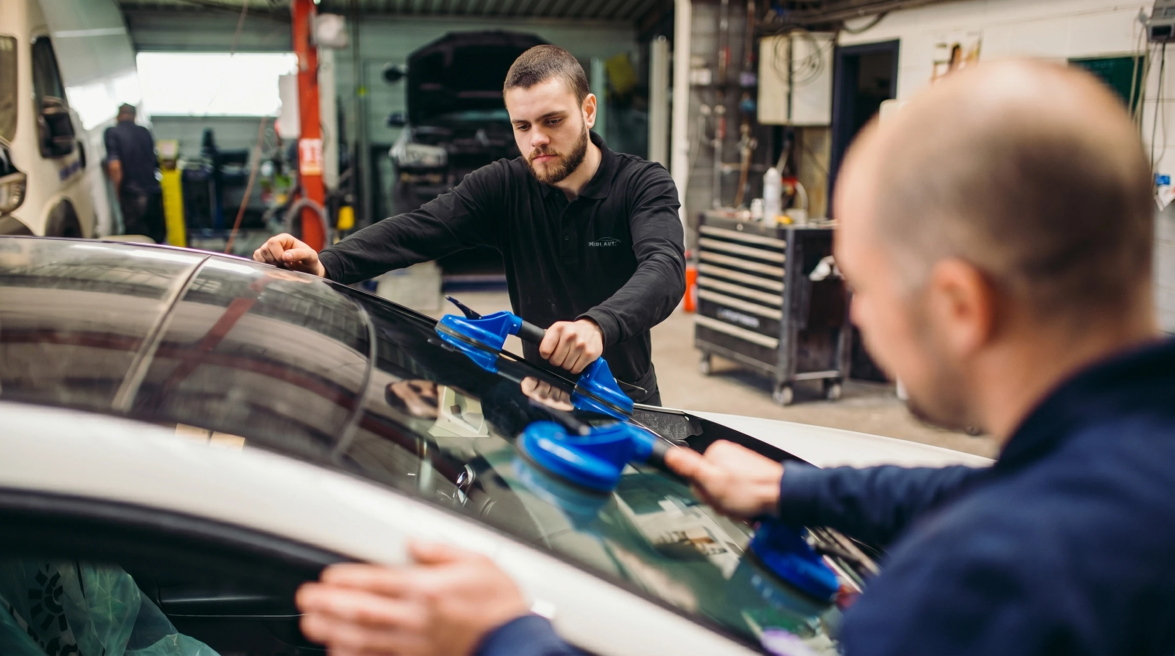 Mécanicien automobile en combinaison bleue travaillant sous le capot ouvert d'une voiture rouge dans un garage professionnel